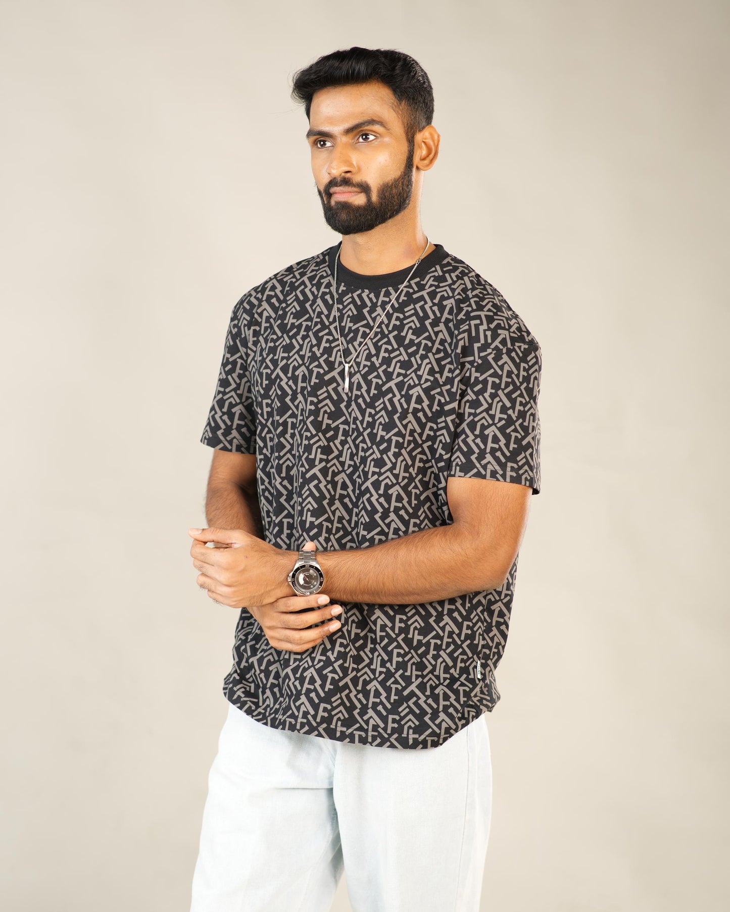 Man wearing a black patterned t-shirt and white pants against a beige background