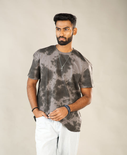 Man wearing a gray tie-dye t-shirt and white pants against a beige background