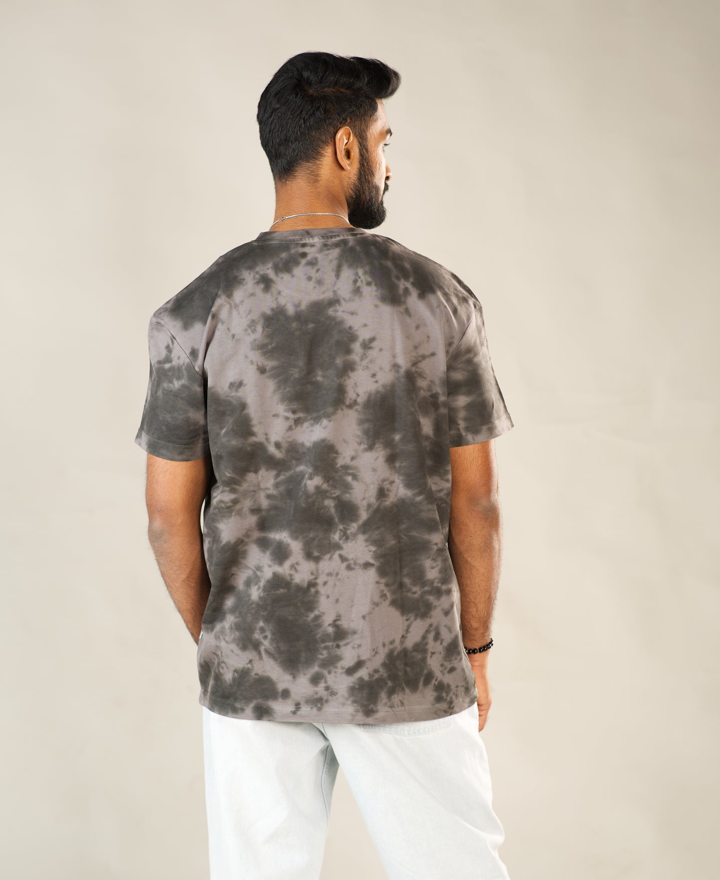 Man wearing a tie-dye t-shirt and white pants on a plain background