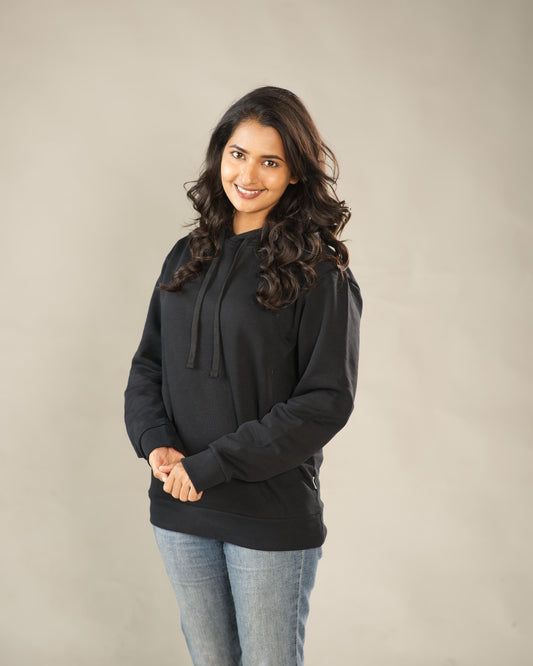 Woman wearing a black hoodie and jeans against a plain background