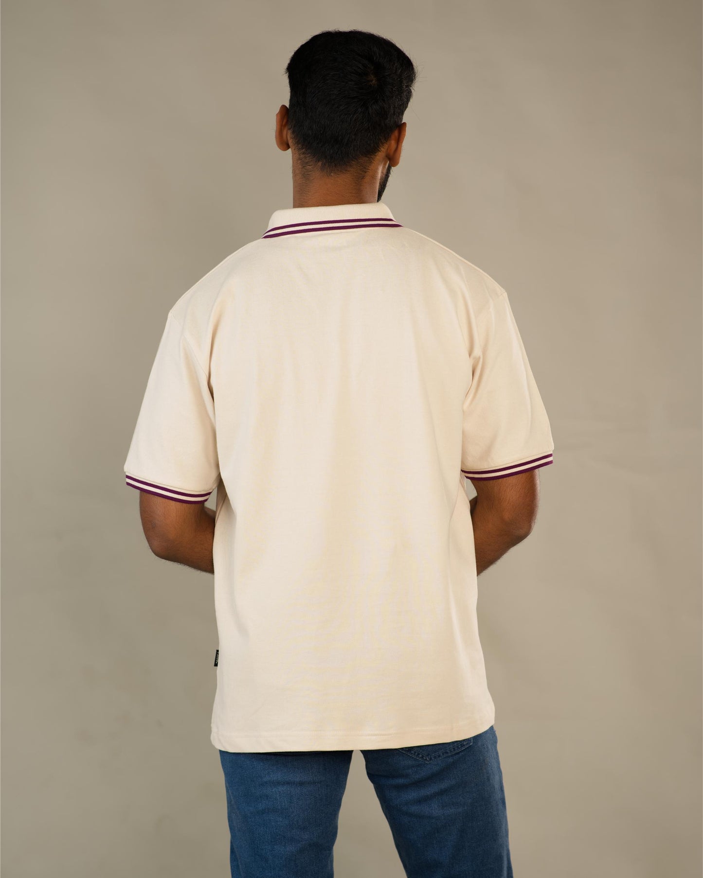 Man wearing a beige polo shirt with red and white trim on a plain background