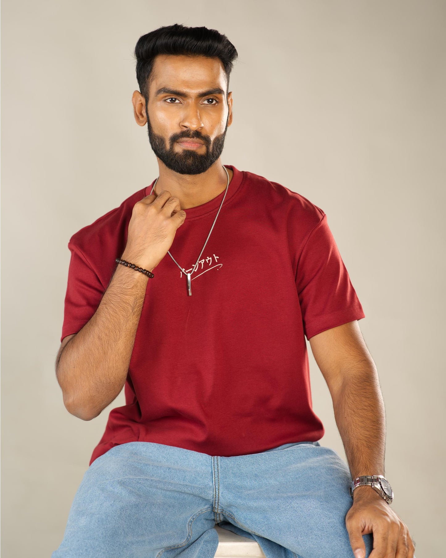 Man wearing a red t-shirt with text and light blue jeans against a beige background