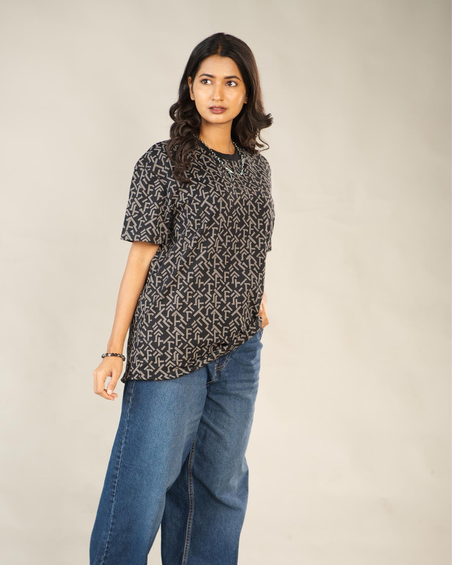 Woman wearing a patterned top and blue jeans against a plain background