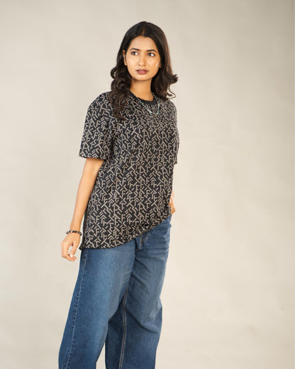 Woman wearing a patterned top and blue jeans against a plain background