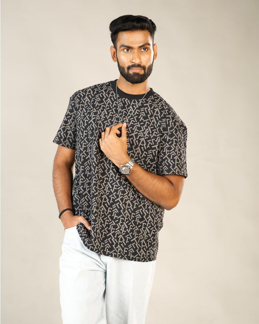 Man wearing a black patterned t-shirt and white pants against a beige background