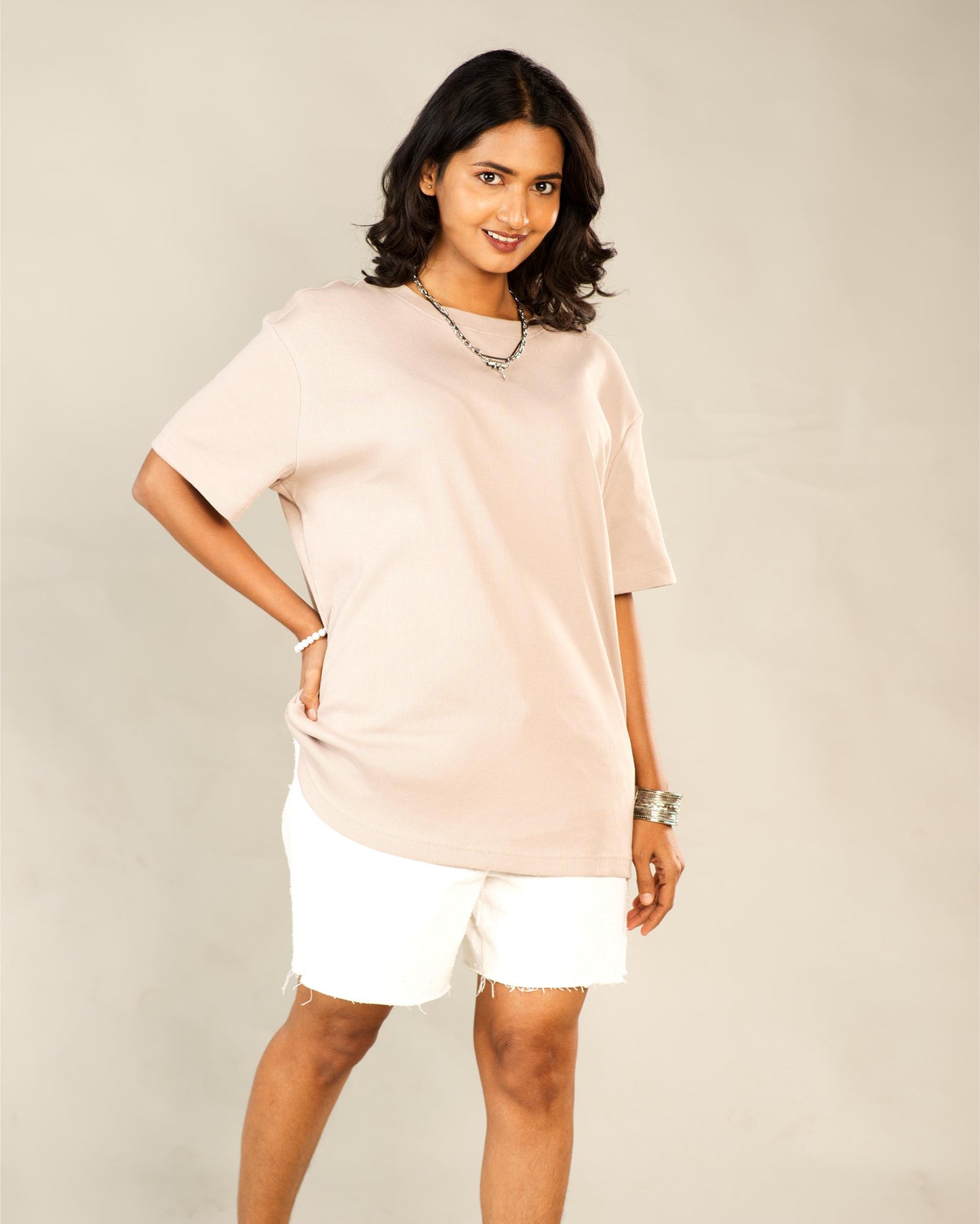 Woman wearing a light pink oversized t-shirt and white shorts against a plain background