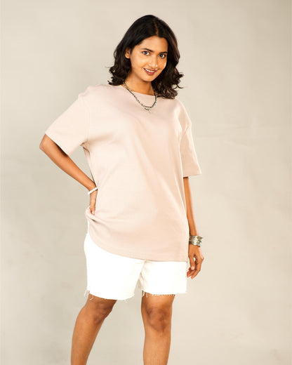 Woman wearing a light pink oversized t-shirt and white shorts against a plain background