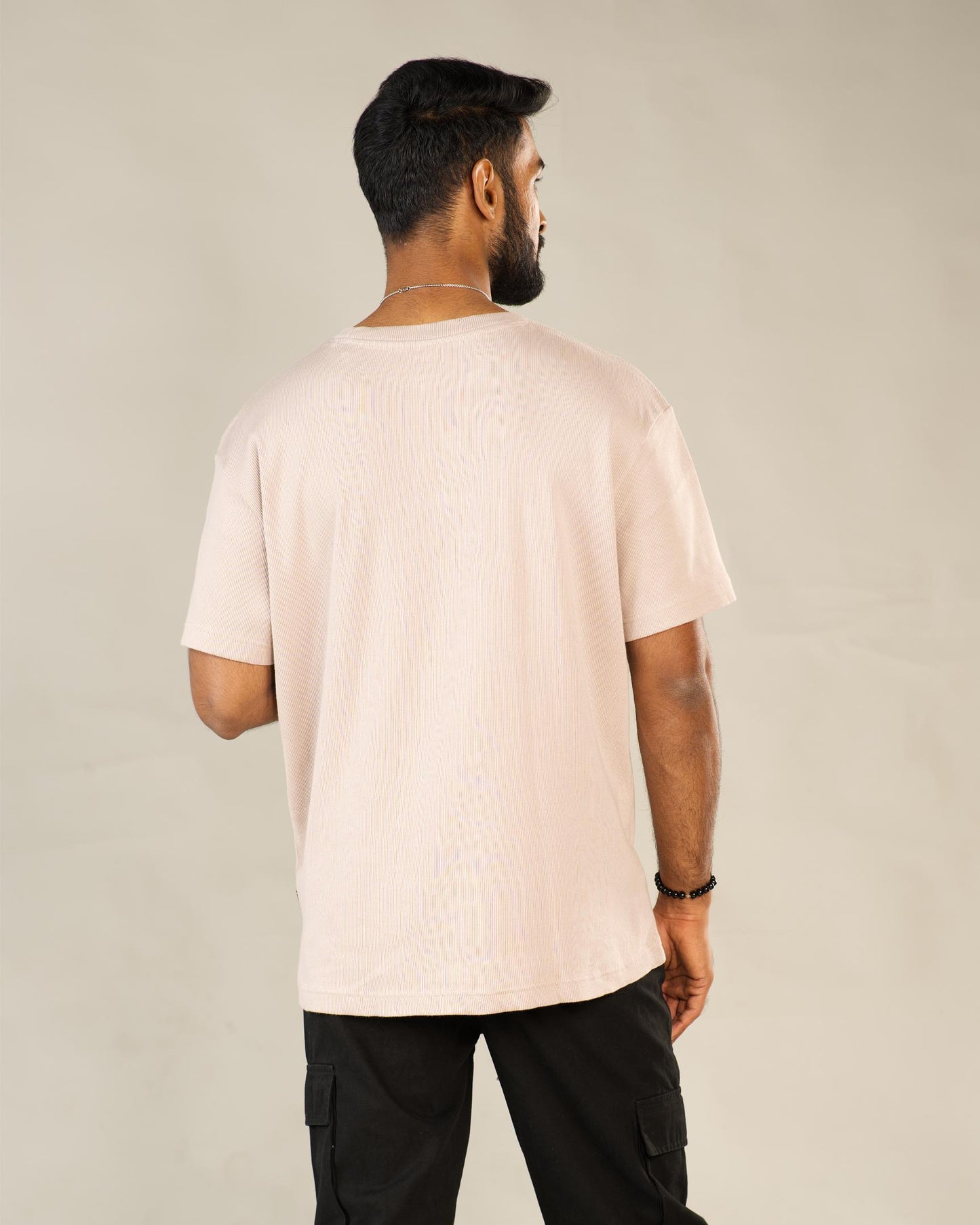 Man wearing a light pink t-shirt and black pants against a plain background