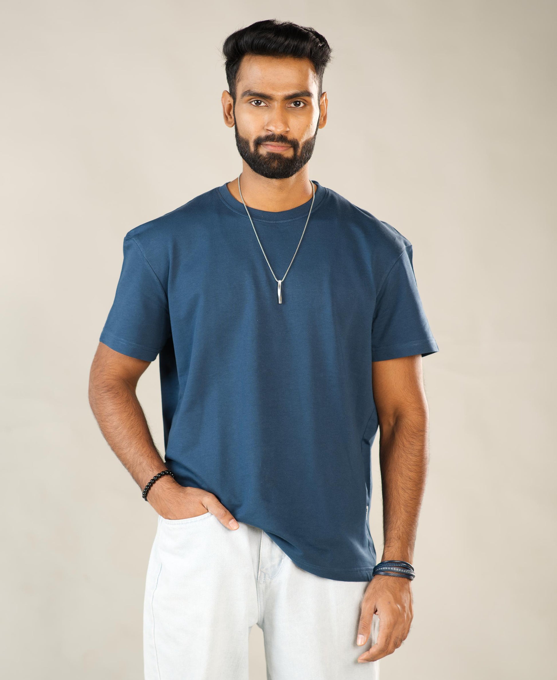 Man wearing a blue t-shirt and white pants against a beige background - Image 1