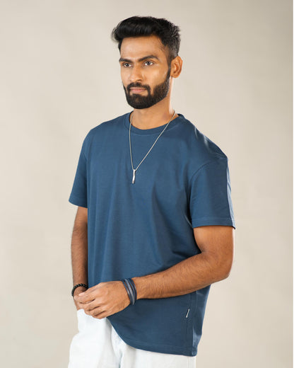 Man wearing a blue t-shirt and white pants against a beige background