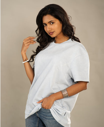Woman wearing a light gray oversized t-shirt and blue jeans against a beige background