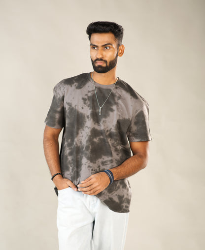 Man wearing a gray tie-dye t-shirt and white pants against a beige background