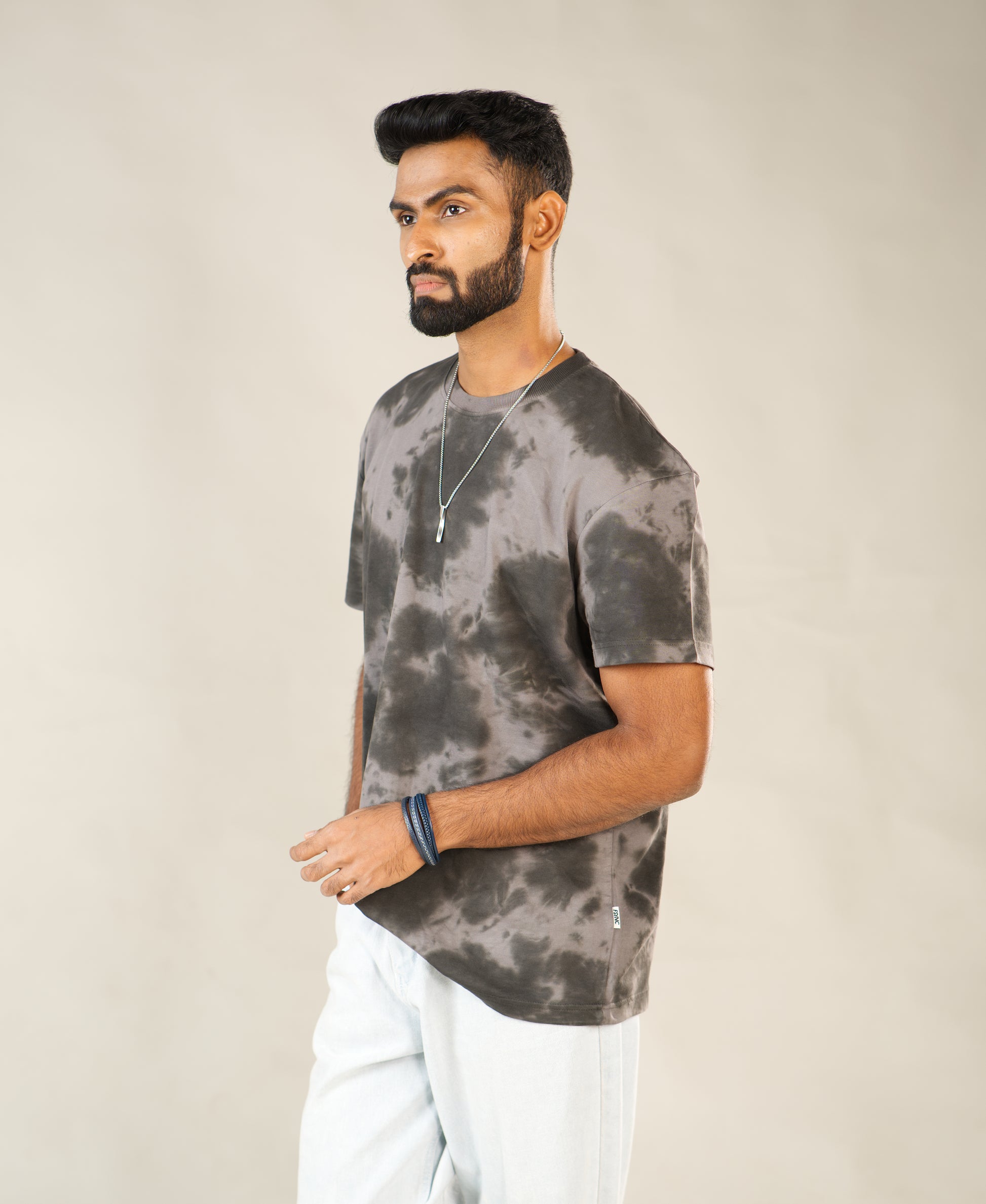 Man wearing a gray tie-dye t-shirt and white pants against a beige background - Image 4