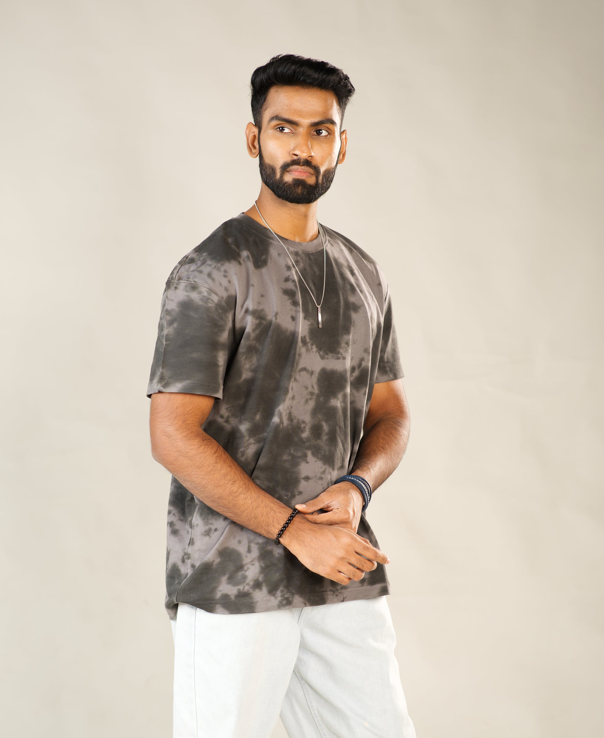 Man wearing a gray tie-dye t-shirt and white pants against a beige background - Image 6