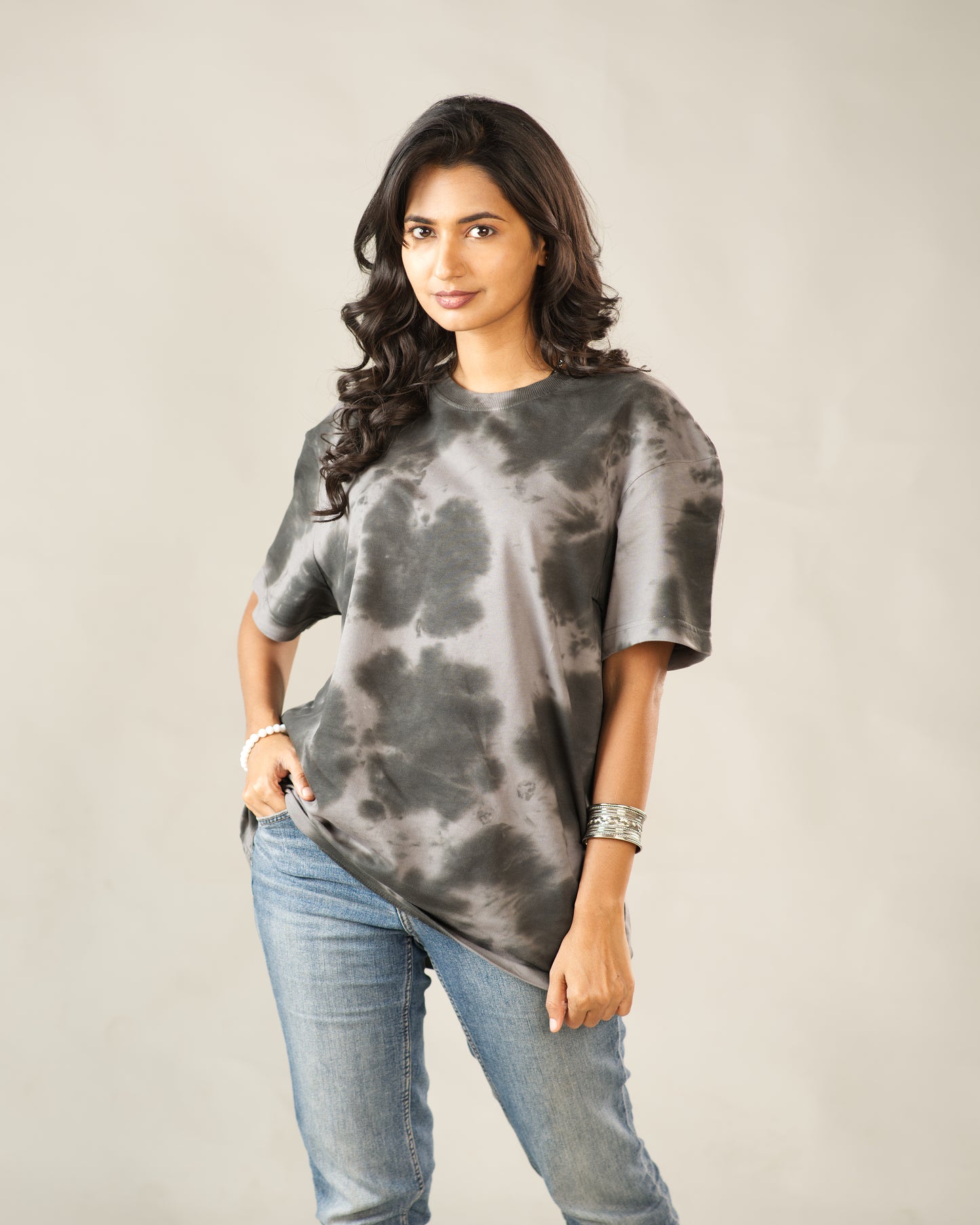 Woman wearing a tie-dye shirt and jeans against a plain background