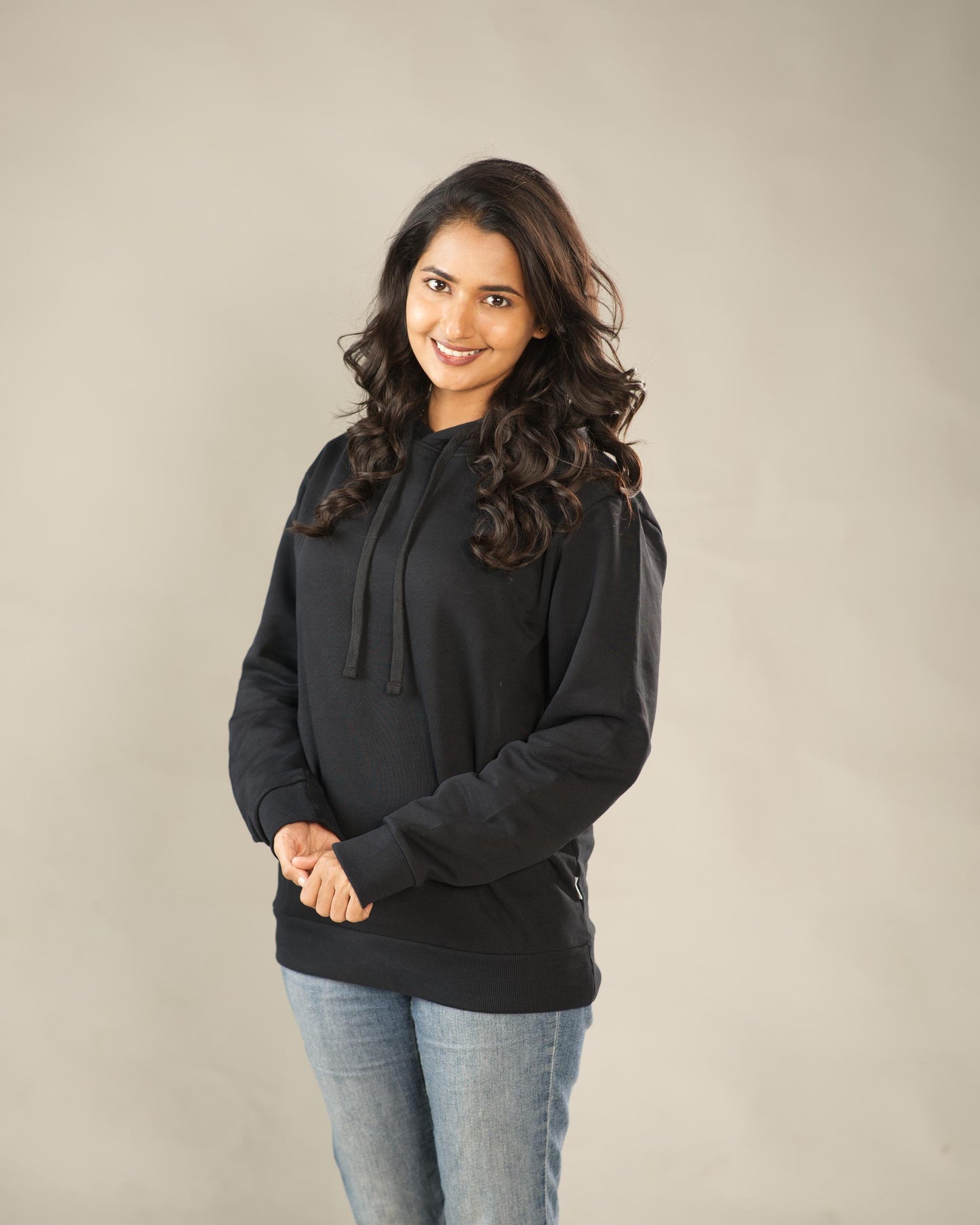 Woman wearing a black hoodie and jeans against a plain background