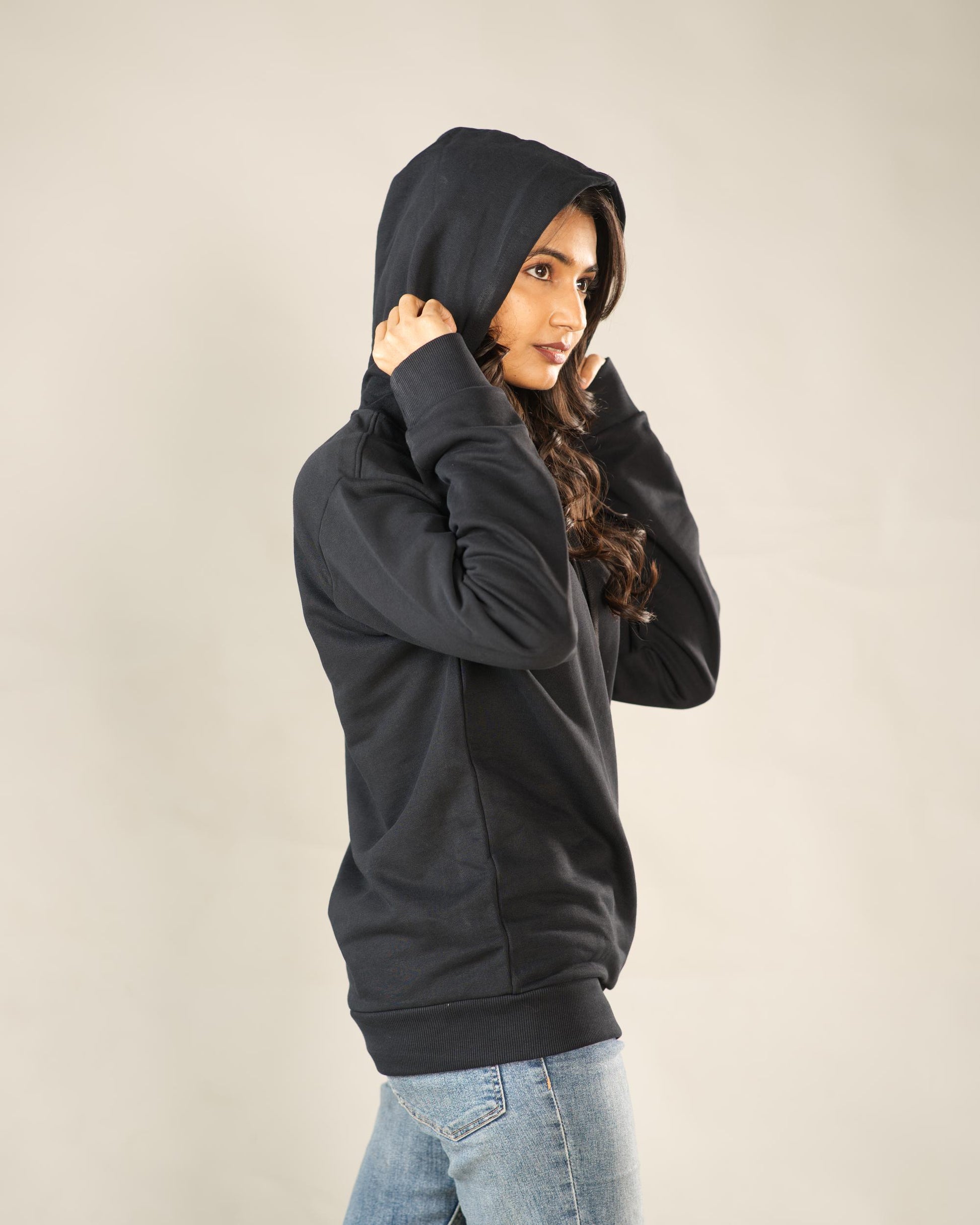 Woman wearing a black hoodie and light blue jeans against a beige background - Image 6