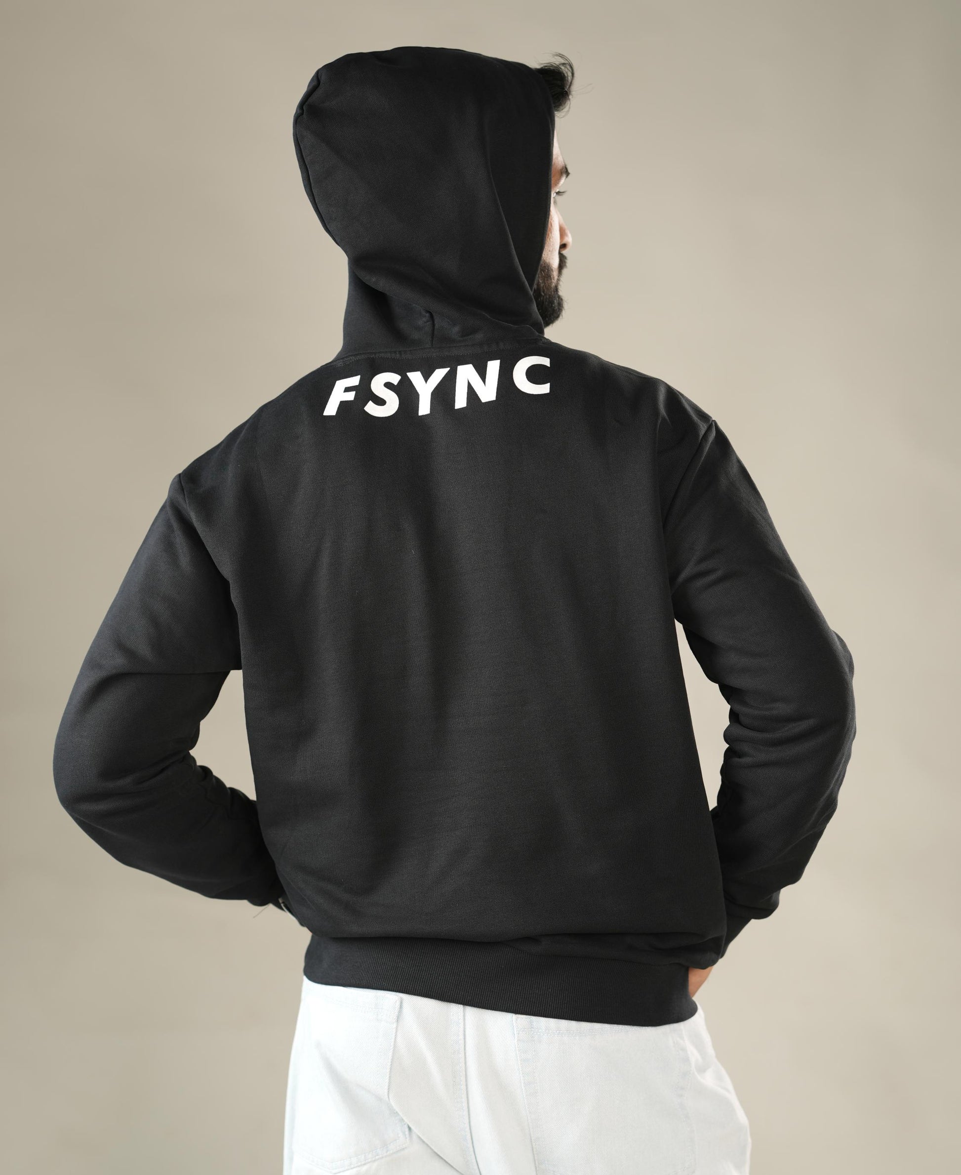Person wearing a black hoodie with 'FSYNC' printed on the back against a beige background - Image 3